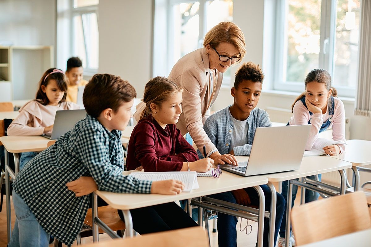 Eine Lehrerin schaut gemeinsam mit Schülerinnen auf ein Laptop.